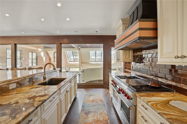 kitchen with light stone countertops, dark hardwood / wood-style flooring, sink, cream cabinets, and range with two ovens