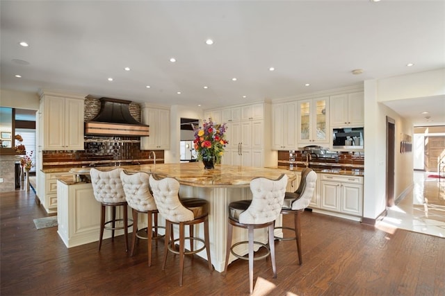 kitchen featuring decorative backsplash, dark hardwood / wood-style flooring, light stone countertops, and custom exhaust hood