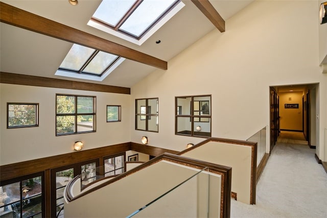 hall featuring a skylight, beamed ceiling, light colored carpet, and high vaulted ceiling