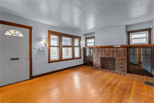 unfurnished living room featuring light wood-type flooring, a brick fireplace, and a wealth of natural light