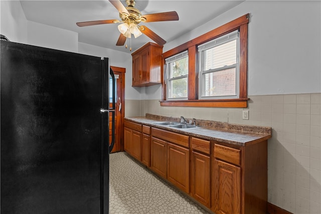 kitchen with ceiling fan, black refrigerator, tile walls, and sink