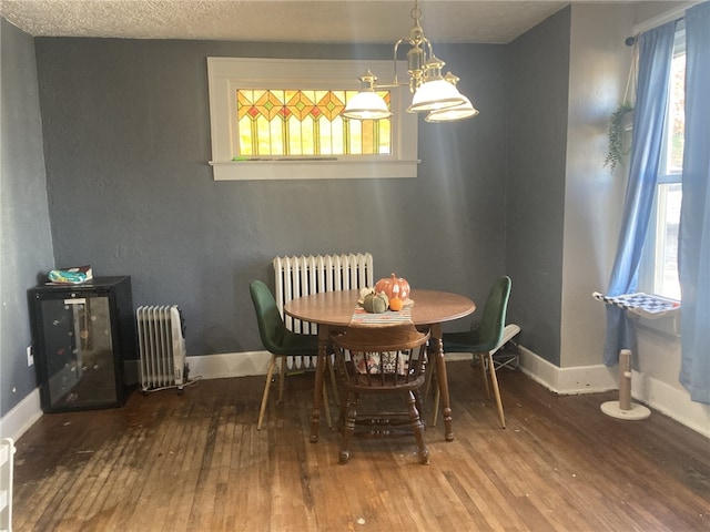 dining space featuring wood-type flooring, a textured ceiling, radiator, and a notable chandelier