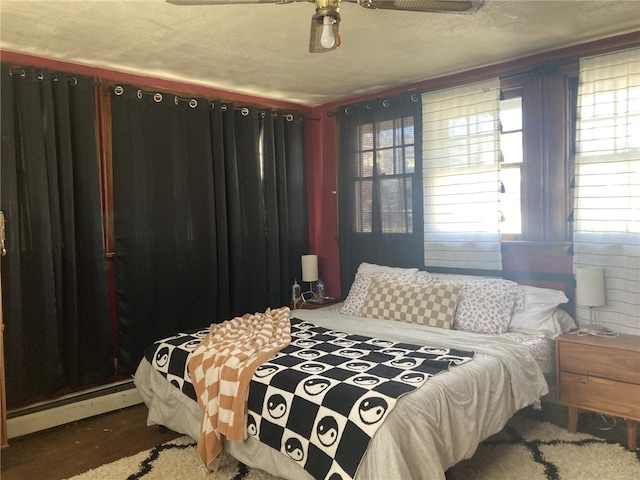 bedroom featuring ceiling fan, wood-type flooring, a textured ceiling, and a baseboard heating unit