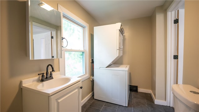 bathroom with tile patterned flooring, vanity, toilet, and stacked washer and clothes dryer