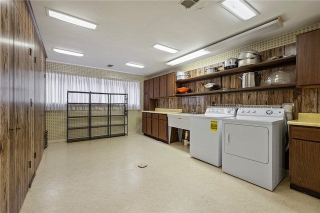 clothes washing area with cabinets, washing machine and dryer, and wooden walls