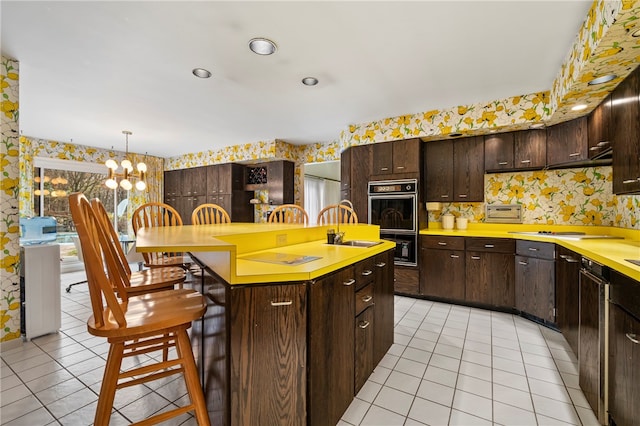 kitchen featuring dark brown cabinetry, an island with sink, a chandelier, a kitchen bar, and light tile patterned floors