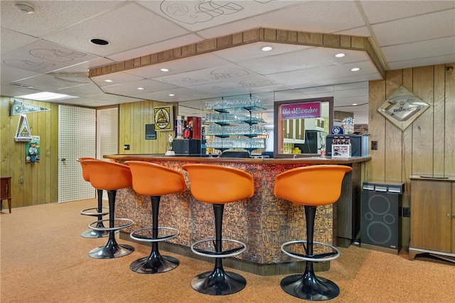 bar with a paneled ceiling, wood walls, and carpet