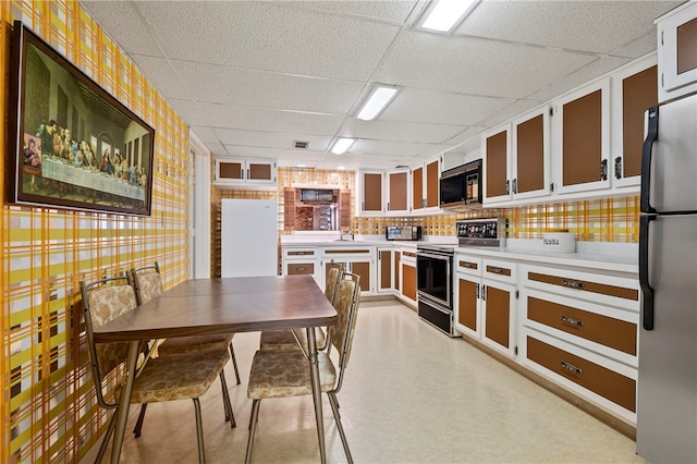 kitchen with a drop ceiling, electric range, white refrigerator, white cabinets, and stainless steel refrigerator