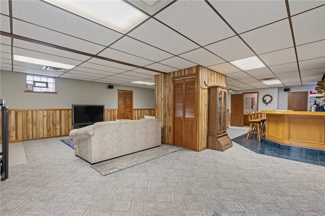 living room with bar area, a paneled ceiling, light colored carpet, and wood walls