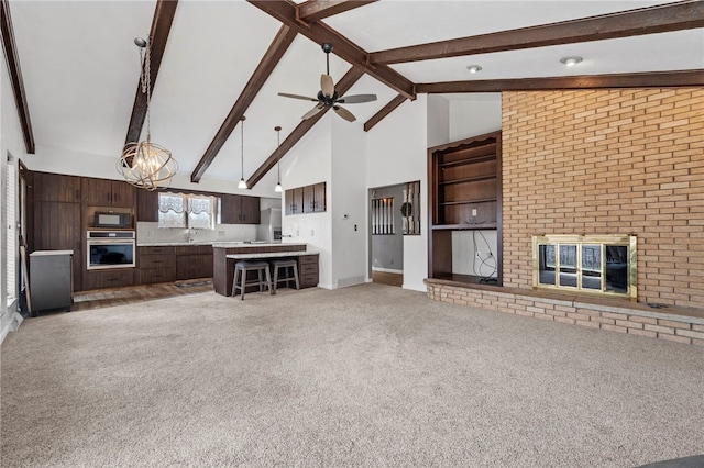 unfurnished living room with carpet flooring, beam ceiling, high vaulted ceiling, a fireplace, and ceiling fan with notable chandelier