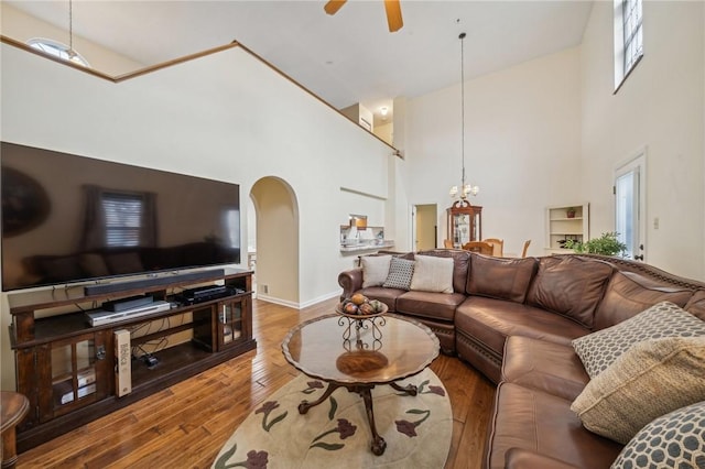 living room with a towering ceiling, wood-type flooring, and ceiling fan with notable chandelier