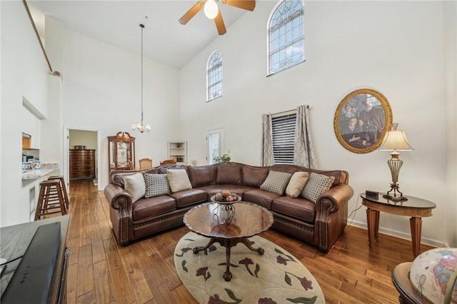 living room featuring ceiling fan with notable chandelier, wood-type flooring, and high vaulted ceiling