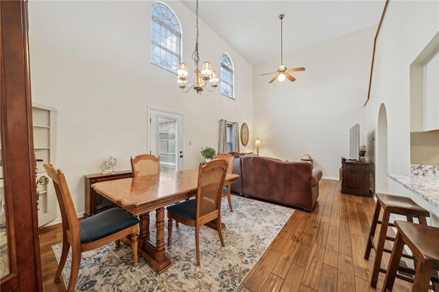 dining area featuring plenty of natural light, ceiling fan with notable chandelier, a high ceiling, and hardwood / wood-style flooring