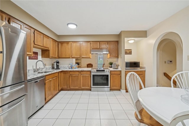 kitchen with light tile patterned floors, stainless steel appliances, light stone counters, and sink