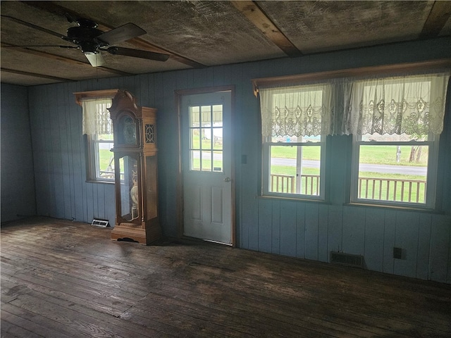 doorway with ceiling fan, dark wood-type flooring, and wooden walls