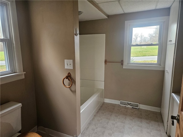 bathroom featuring a paneled ceiling, a bath, and toilet