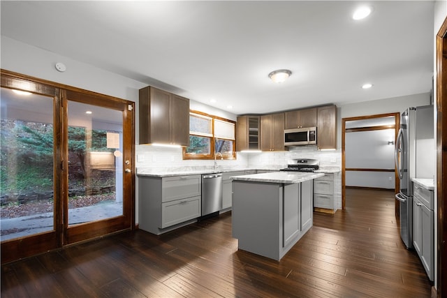 kitchen featuring stainless steel appliances, light stone counters, dark hardwood / wood-style floors, backsplash, and a kitchen island