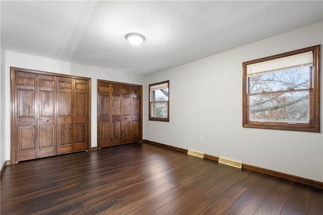 unfurnished bedroom with dark wood-type flooring, multiple windows, and two closets