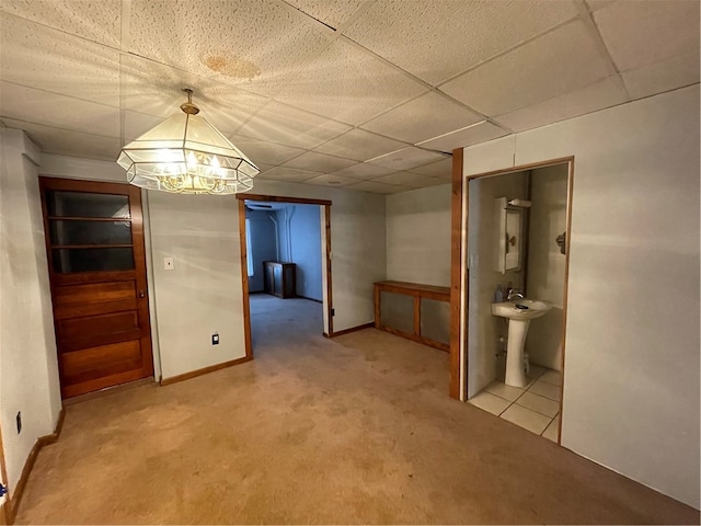 unfurnished dining area featuring a drop ceiling, sink, light carpet, and a chandelier