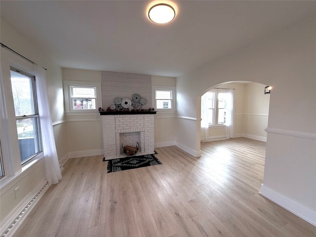 unfurnished living room with a baseboard heating unit, light wood-type flooring, a brick fireplace, and a healthy amount of sunlight