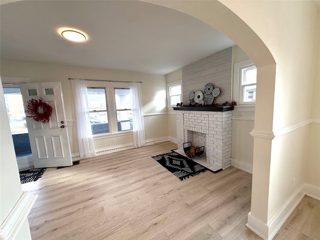 living room with a healthy amount of sunlight, light wood-type flooring, a baseboard radiator, and a brick fireplace