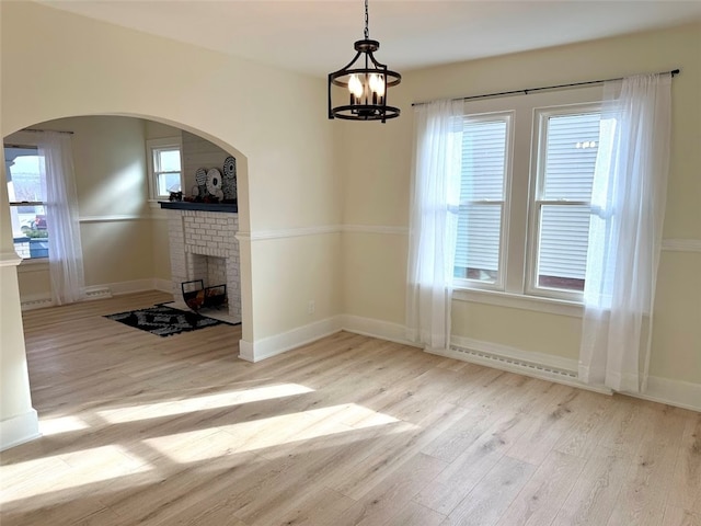 unfurnished dining area with a notable chandelier, a fireplace, a wealth of natural light, and light hardwood / wood-style flooring