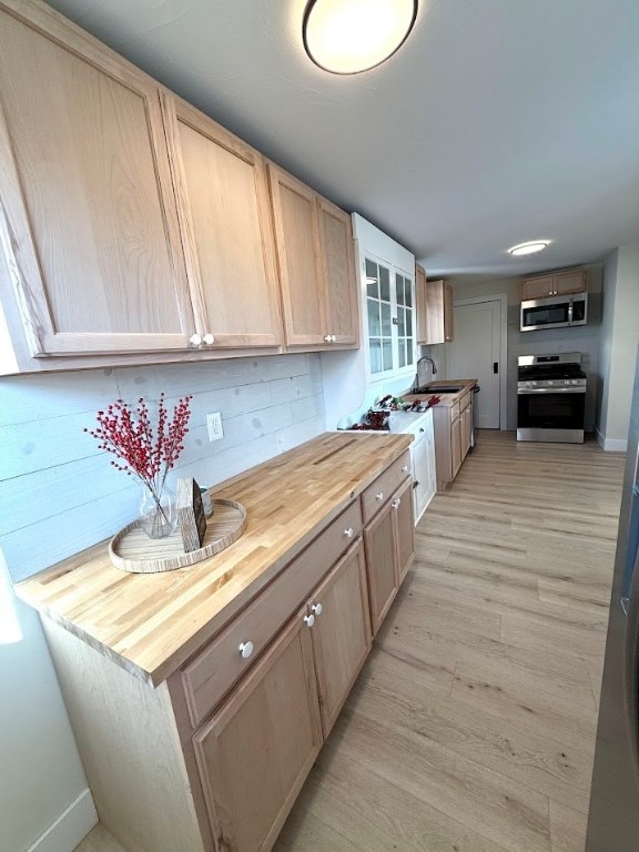 kitchen with butcher block counters, light brown cabinets, stainless steel appliances, and light wood-type flooring