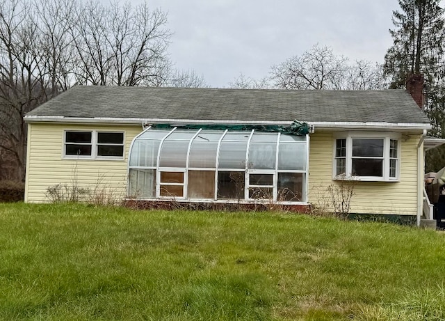 rear view of property with a shingled roof, a yard, and a chimney