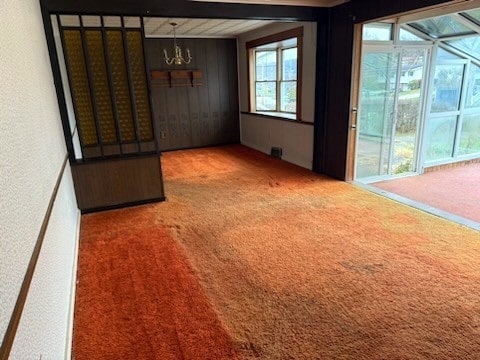 unfurnished room with carpet flooring, a notable chandelier, and beam ceiling