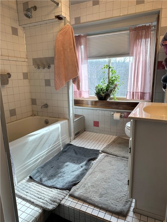 full bathroom with vanity, tile patterned floors, tiled shower / bath combo, toilet, and tile walls