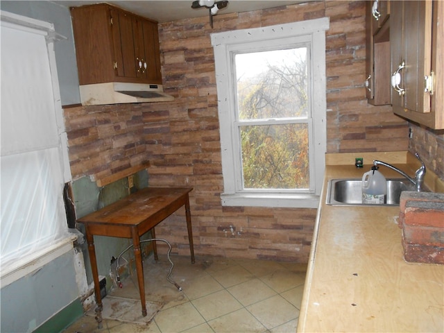 kitchen featuring wooden walls, sink, light tile patterned floors, and a healthy amount of sunlight