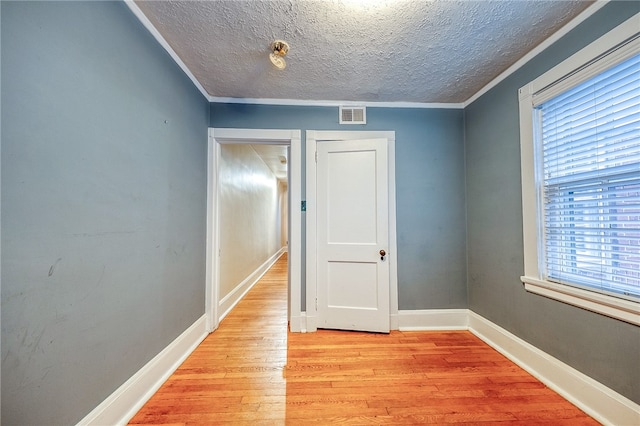 spare room with light hardwood / wood-style flooring, a textured ceiling, and ornamental molding