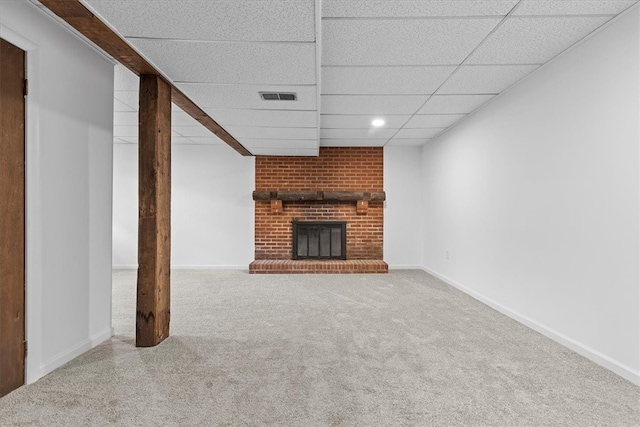 unfurnished living room featuring carpet flooring, a drop ceiling, and a brick fireplace