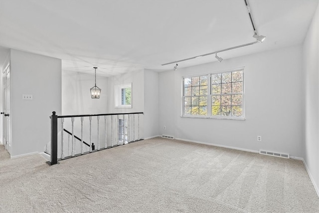 spare room with carpet, track lighting, and a notable chandelier