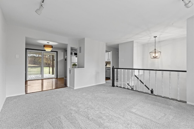 carpeted empty room featuring track lighting and an inviting chandelier