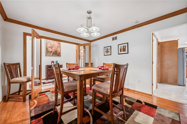 dining room with light wood-type flooring, ornamental molding, and a chandelier