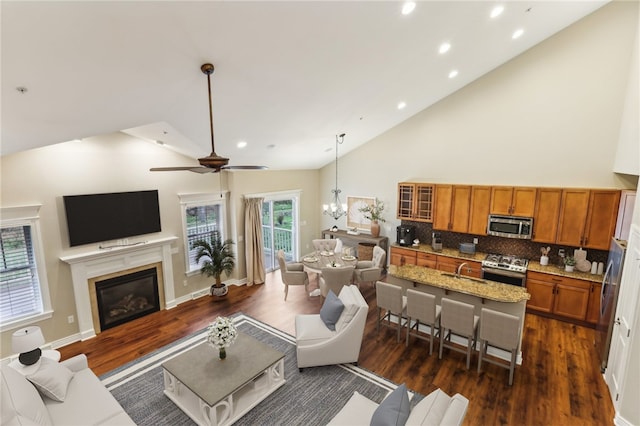 living room featuring high vaulted ceiling, dark hardwood / wood-style floors, sink, and ceiling fan with notable chandelier