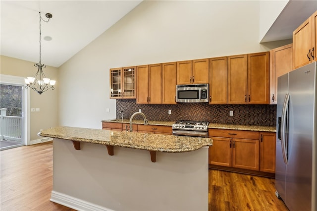 kitchen featuring a kitchen bar, appliances with stainless steel finishes, dark hardwood / wood-style flooring, light stone countertops, and decorative light fixtures