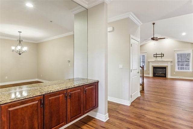 kitchen featuring lofted ceiling, dark hardwood / wood-style floors, ornamental molding, decorative light fixtures, and light stone counters