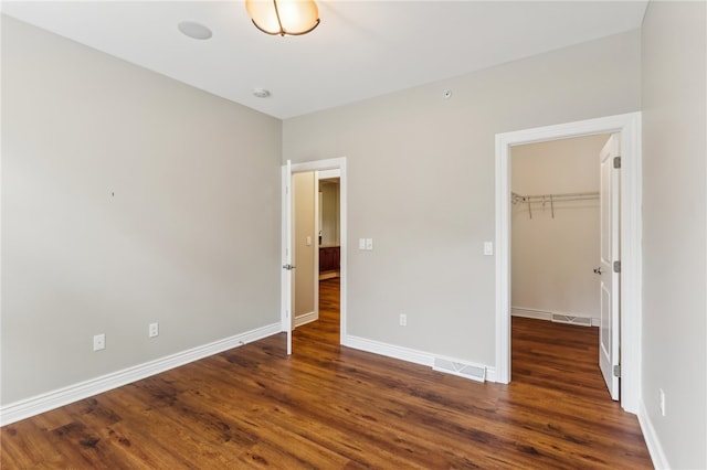 unfurnished bedroom with a closet, a spacious closet, and dark hardwood / wood-style flooring