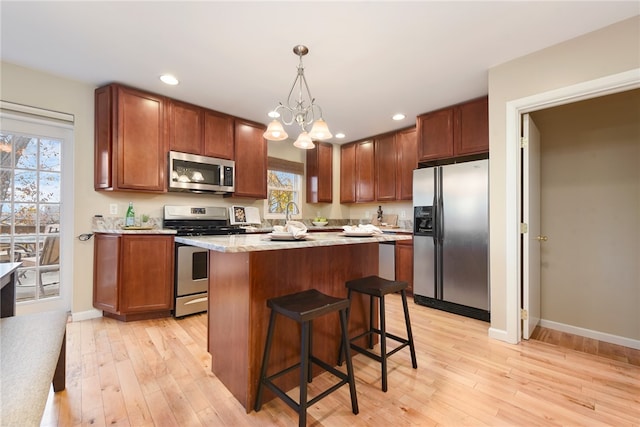 kitchen featuring appliances with stainless steel finishes, light wood-type flooring, decorative light fixtures, a chandelier, and a center island