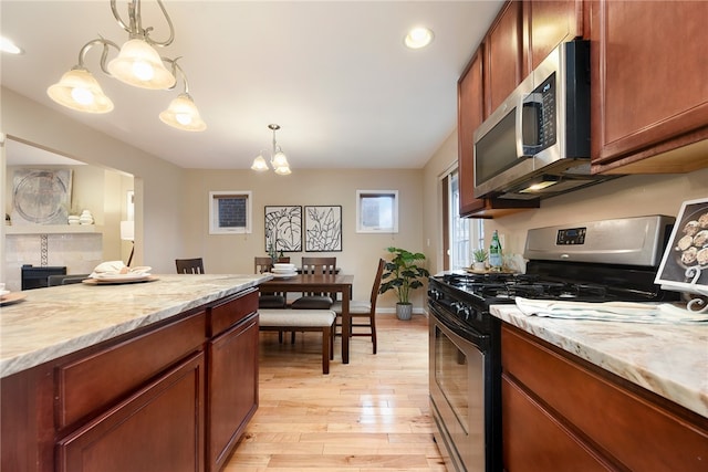 kitchen with appliances with stainless steel finishes, an inviting chandelier, light hardwood / wood-style flooring, and pendant lighting