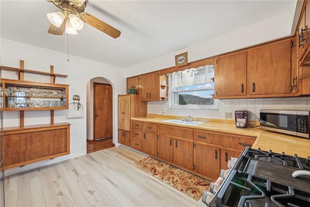 kitchen with ceiling fan, sink, backsplash, appliances with stainless steel finishes, and light wood-type flooring