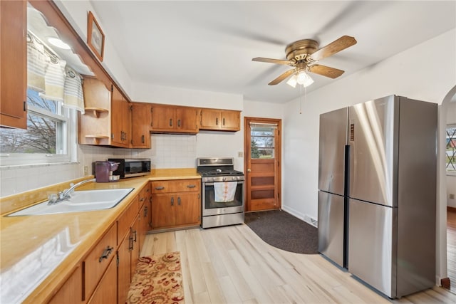 kitchen with ceiling fan, sink, stainless steel appliances, tasteful backsplash, and light wood-type flooring