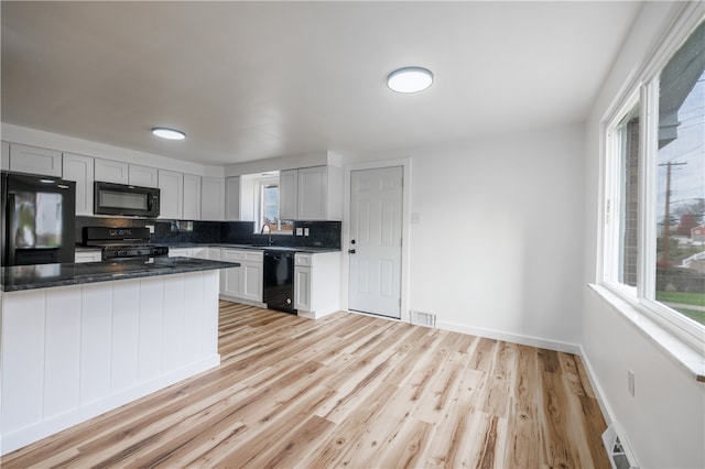 kitchen featuring backsplash, light hardwood / wood-style floors, white cabinetry, and black appliances