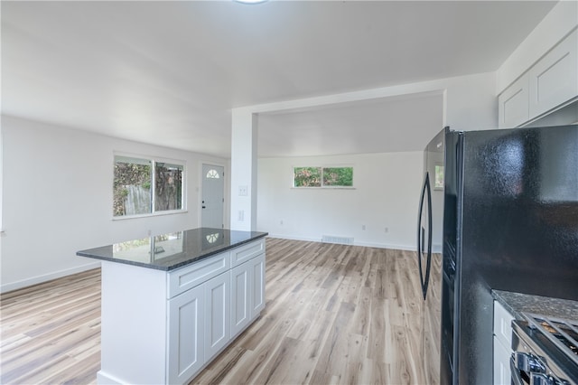 kitchen with white cabinetry, black fridge, dark stone countertops, vaulted ceiling, and light wood-type flooring