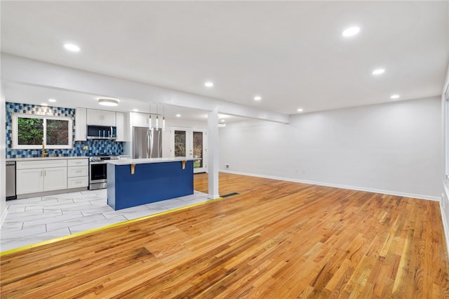 kitchen with white cabinetry, stainless steel appliances, a kitchen breakfast bar, light hardwood / wood-style floors, and a kitchen island