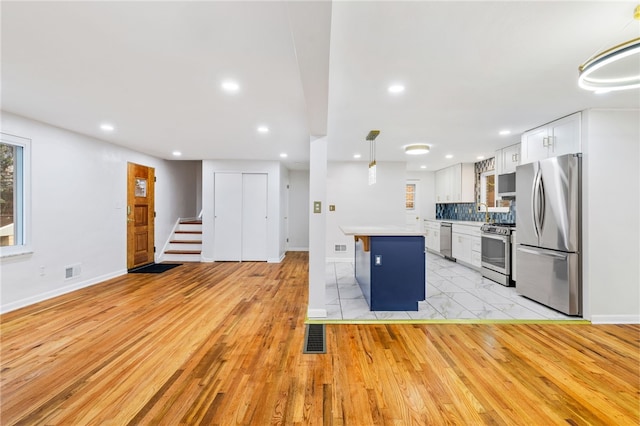 kitchen with a center island, hanging light fixtures, light hardwood / wood-style floors, white cabinets, and appliances with stainless steel finishes