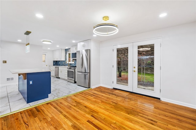 kitchen with french doors, stainless steel appliances, pendant lighting, white cabinets, and a breakfast bar area