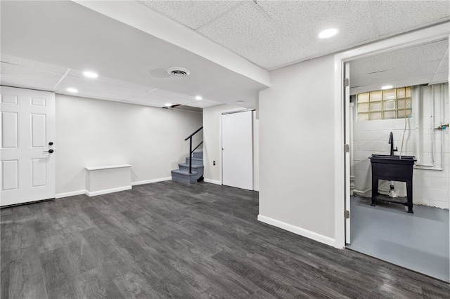 basement with a drop ceiling and dark wood-type flooring